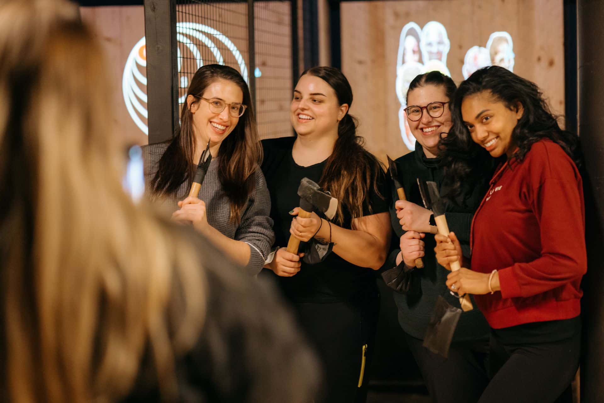 Group of girls pose with their axes in front of the throwing lanes at AXED Throwing.