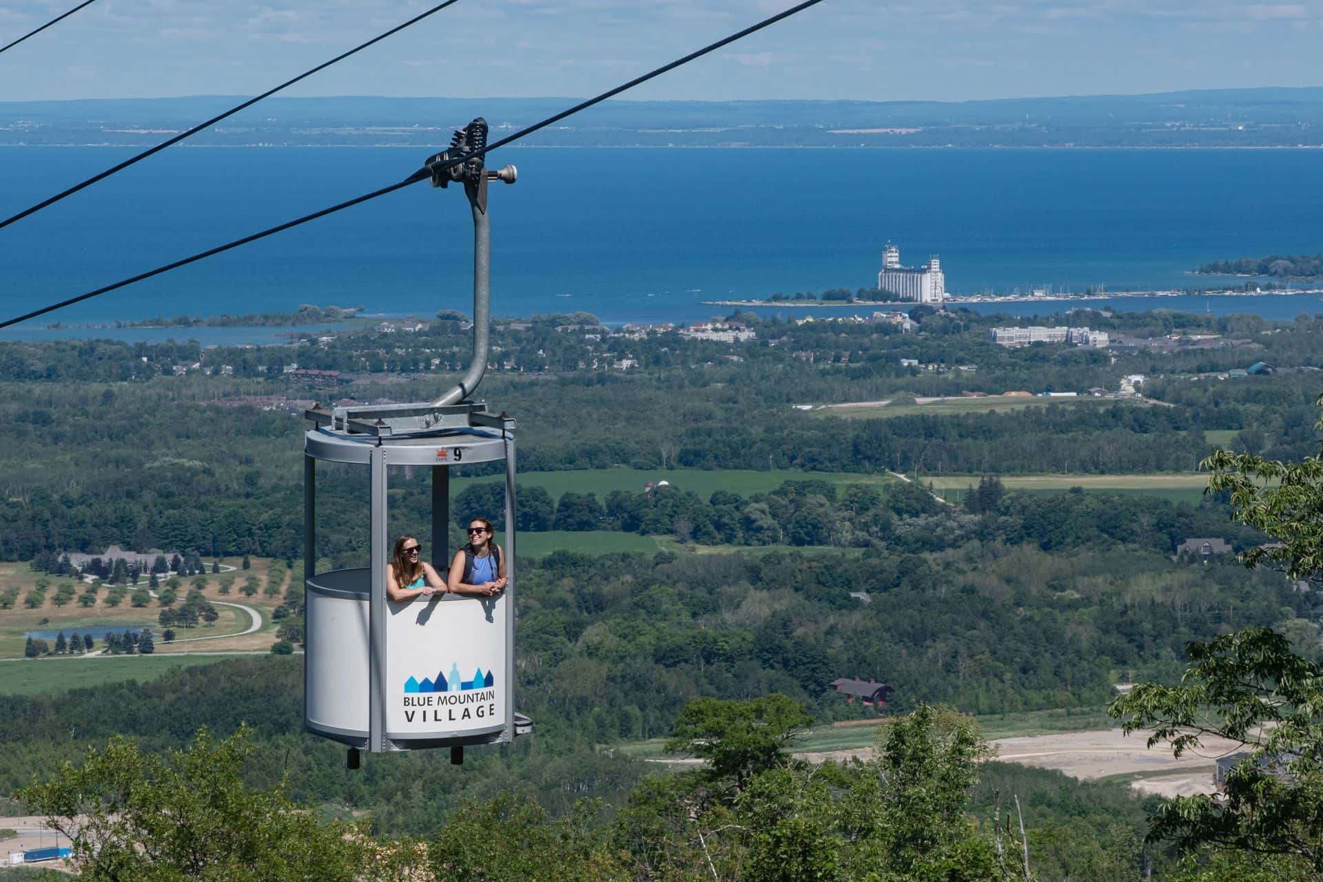 Two friends riding up the gondola in the summer with Georgian Bay as a backdrop.
