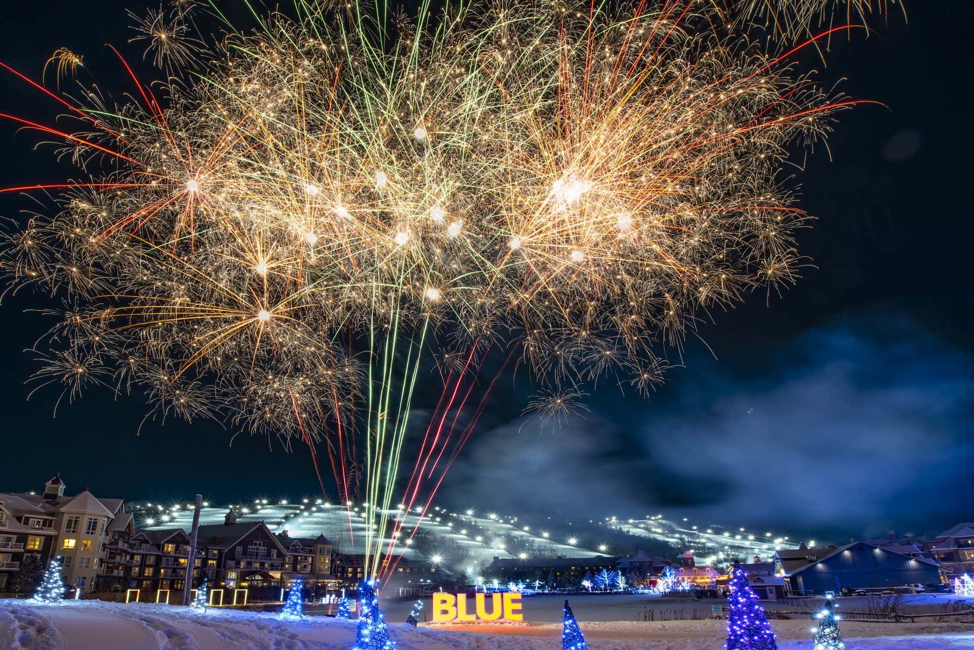 Fireworks bursting over the lit up Village and snow covered Mountain for New Years Eve at Blue