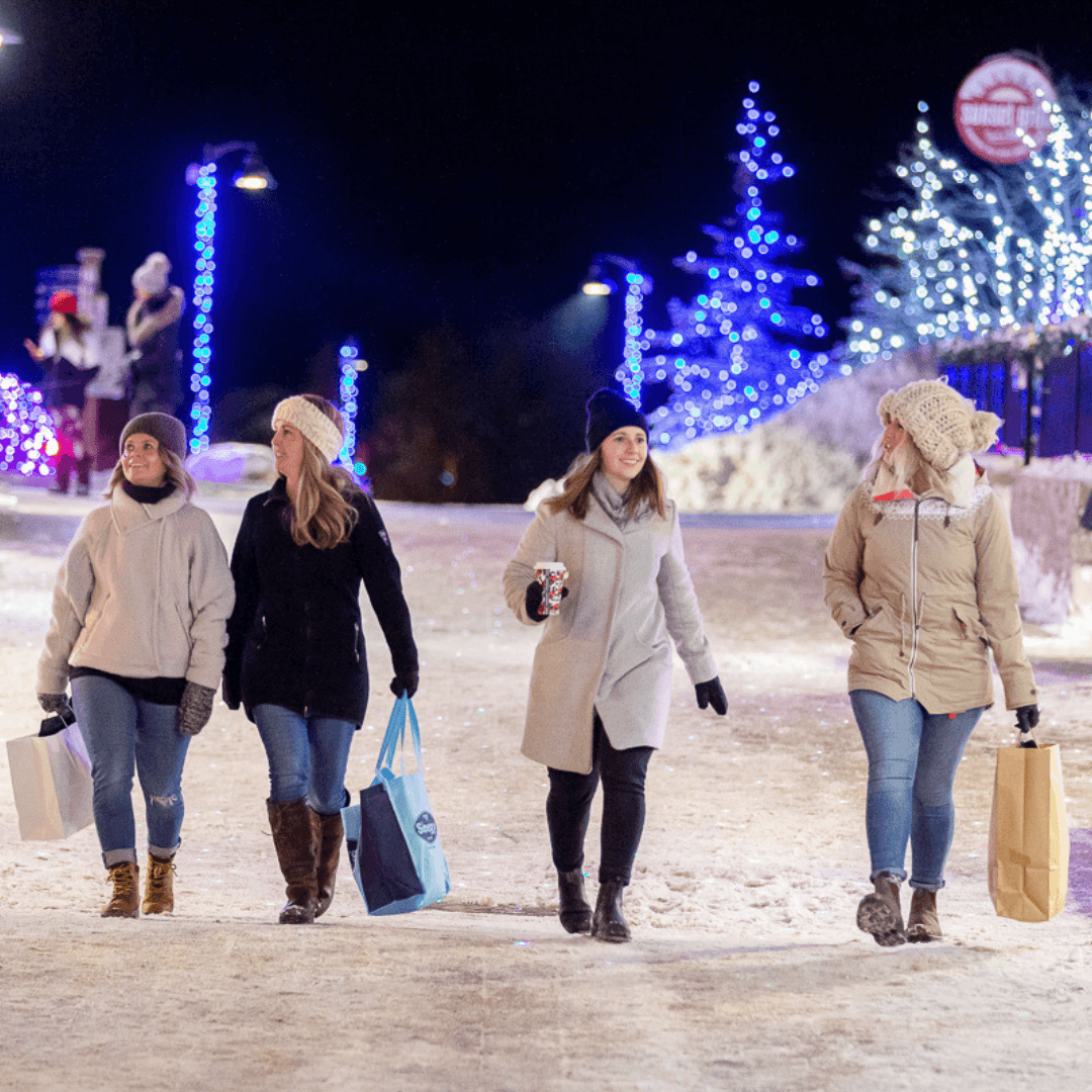 Group of friends shopping in the village at night, with the streets illuminated with holiday lights.