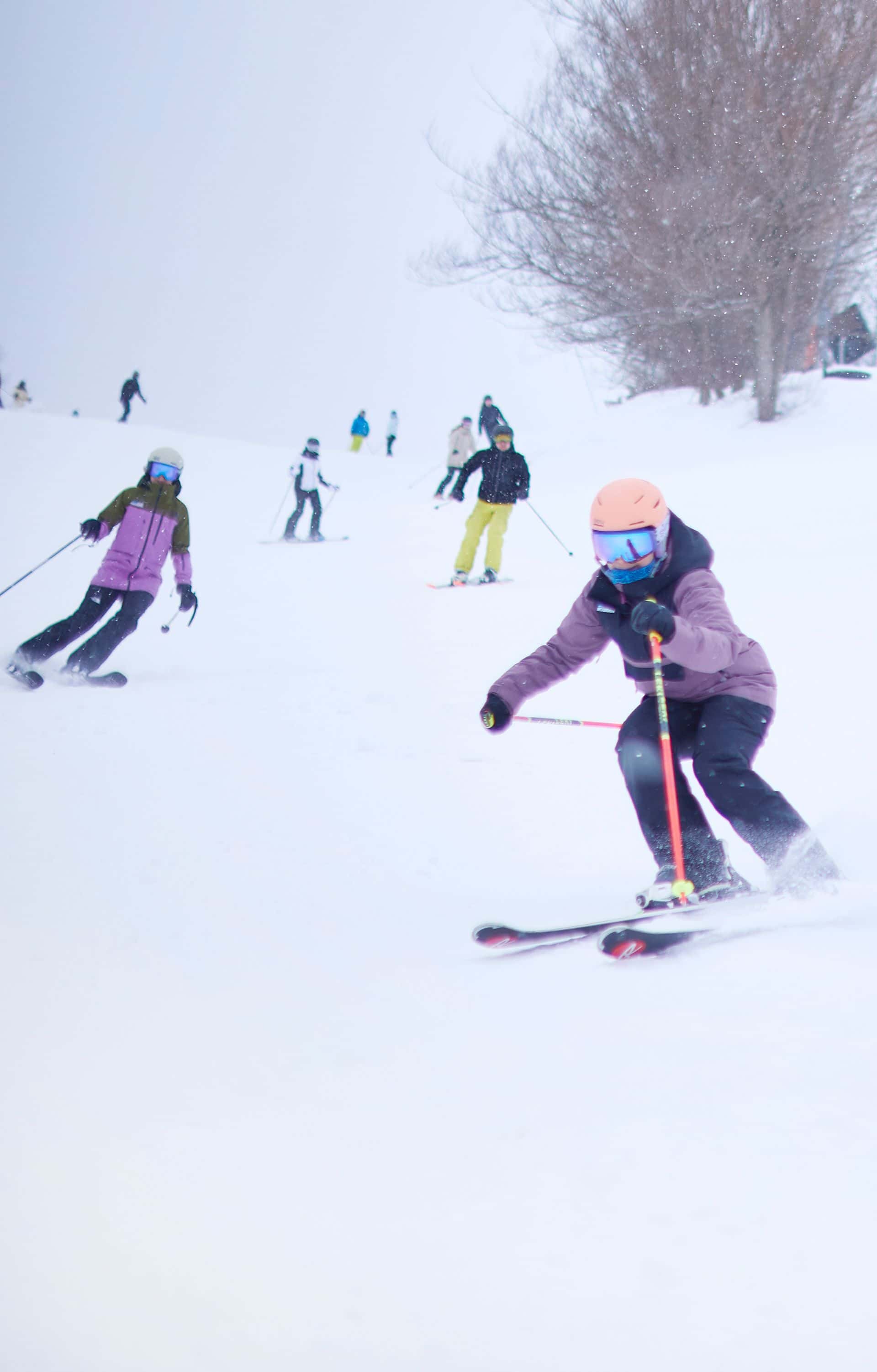 Group of friends race each other down the ski slopes on a snowy Winter afternoon.