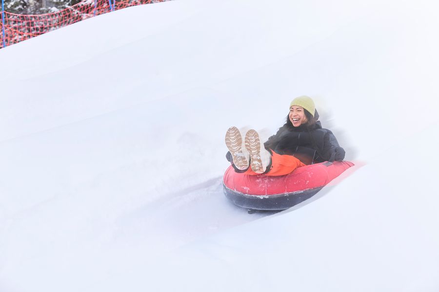 Woman in a snow tube, smiling wide as she speeds down the snow covered slope.