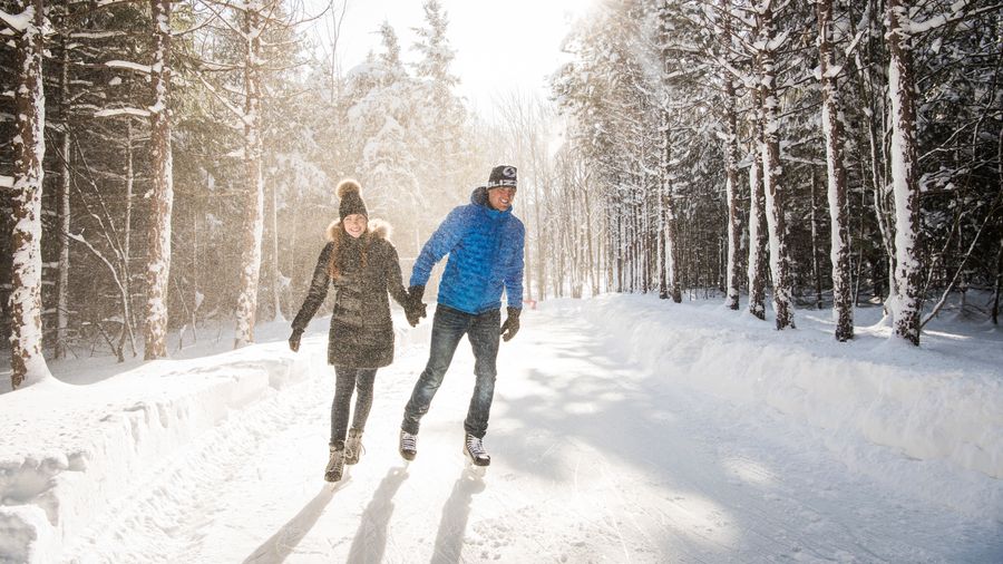 Couple holding hands and skating around the 1.1km ice skating loop at the top of the Mountain on a snowy winter's day.