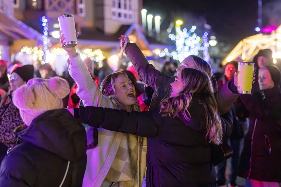Closeup of two friends among a crowd of people, dancing and singing to live music in the Village Events Plaza
