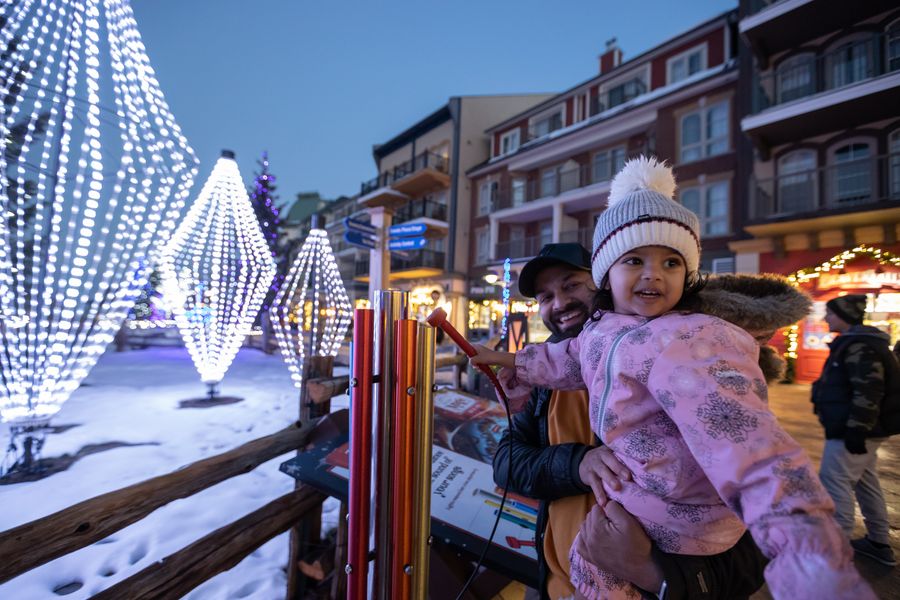 Father holding up his toddler daughter to play the interactive musical maestro light activation along the Holiday Magic Light Trail.