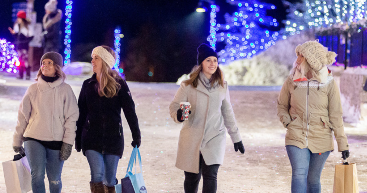 Group of friends shopping in the village at night, with the streets illuminated with holiday lights.
