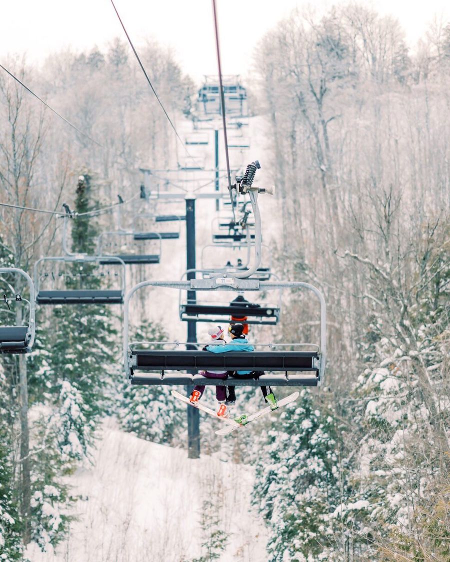 Couple equip for snowboarding, riding up the chairlift with a view of the mountain on a snowy Winter's day.