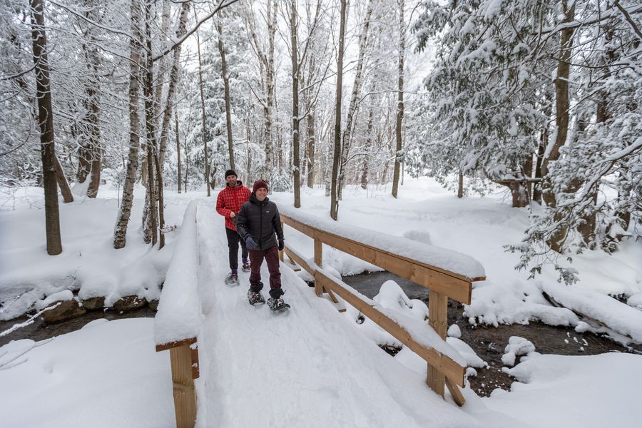 A male couple snowshoeing across a snow covered bridge, along the mountain top snowshoeing trail.