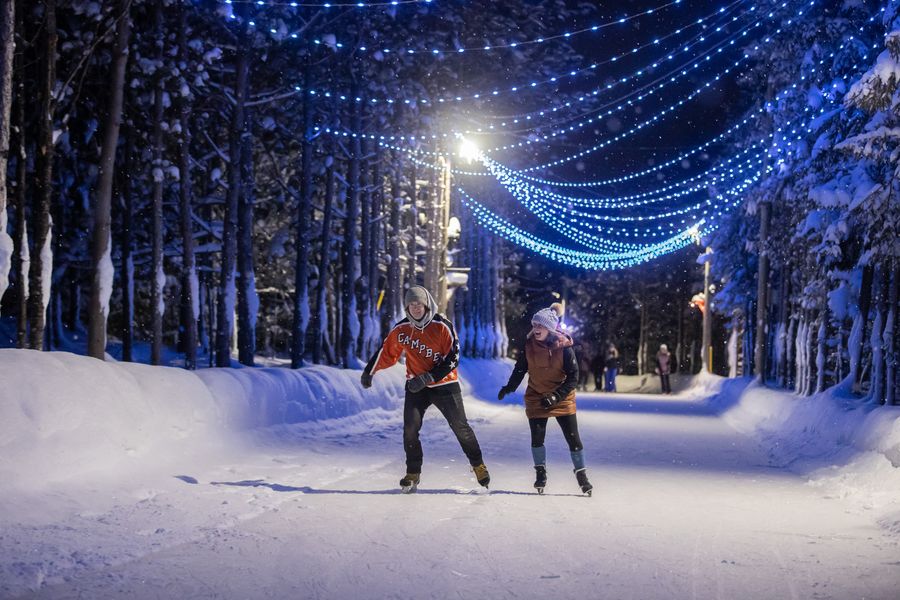 A couple races each other on ice skates as they glide along the festively lit Woodview Mountaintop Skating Loop.