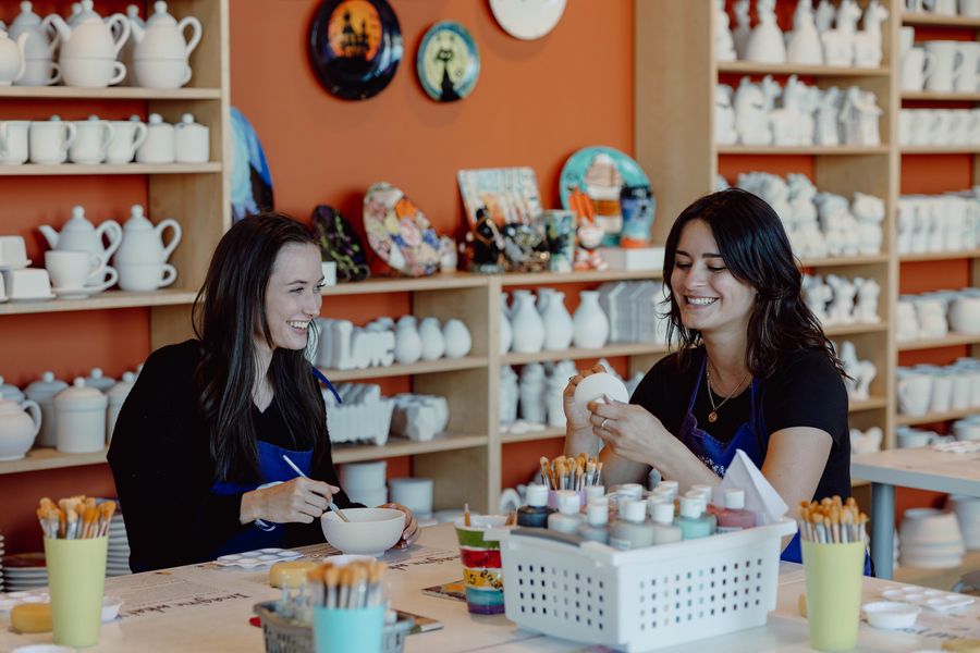 Two friends painting their own pottery at Crock-a-Doodle studio in the Village.
